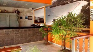 A reception area with a stone counter, a large potted plant, and a mural of a mountainous landscape. - Hotel Pousada Miramar (Ubatuba)