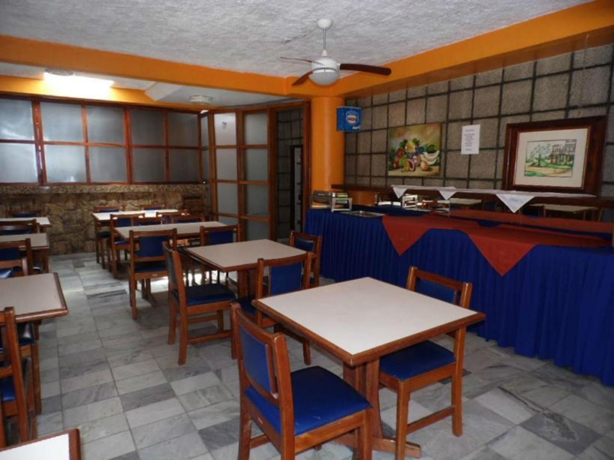 Un restaurante con mesas de madera y sillas con cojines azules, suelo de baldosas y una pared de piedra con un cuadro.