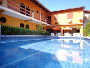 A swimming pool with lounge chairs and umbrellas, surrounded by a building with a yellow facade and balconies. - Hotel Pousada Miramar (Ubatuba)