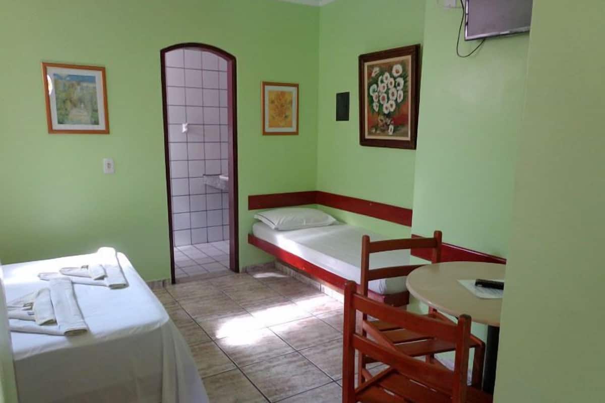 A small, green-walled room with a single bed, a chair, and a table.
