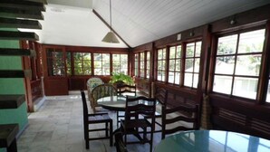 A dining area with a round table and chairs, large windows, and a ceiling with wooden beams. - Hotel Pousada Miramar (Ubatuba)