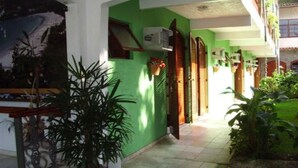 A building with a green facade, a tiled entrance, and a small garden area with potted plants. - Hotel Pousada Miramar (Ubatuba)