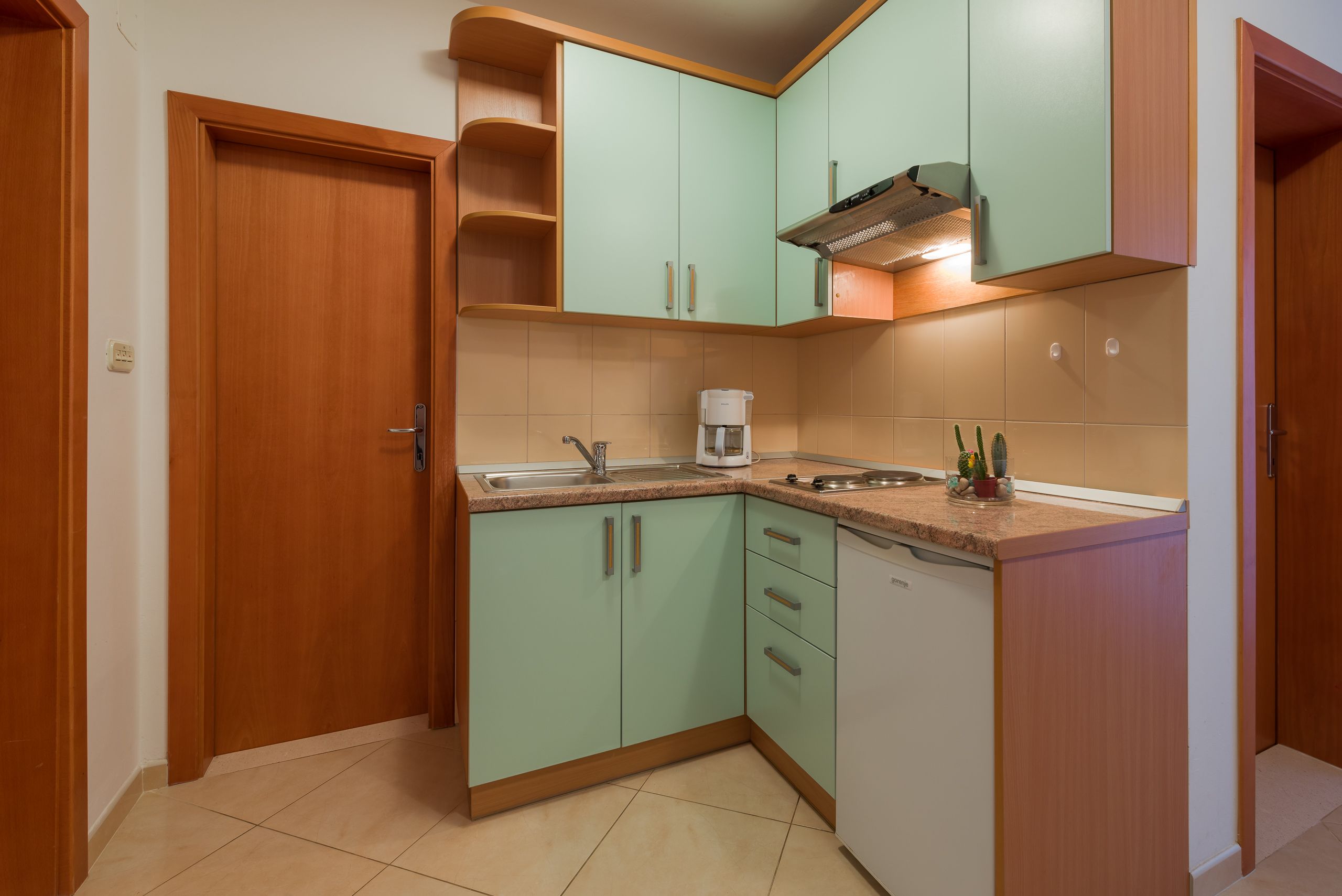 A compact kitchen with light green cabinets, a built-in dishwasher, and a coffee maker.