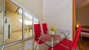 Un espace repas moderne avec une table en verre et des chaises rouges, un vase rempli de fleurs jaunes et une vue sur une terrasse extérieure.