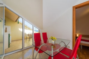 A modern dining area with a glass table and red chairs, a vase with yellow flowers, and a view of an outdoor patio. - Villa Vallum (Bol)