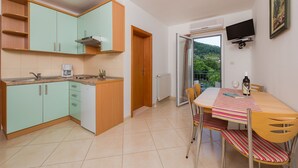 Une cuisine de taille réduite avec des meubles de couleur turquoise, un plan de travail en bois et un coin repas agrémenté d’une nappe à rayures.