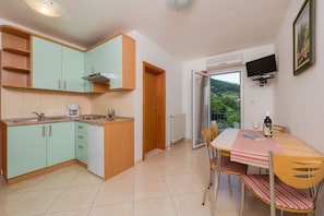 A compact kitchen with teal cabinets, a wooden countertop, and a dining area with a striped tablecloth. - Villa Vallum (Bol)