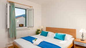 Un lit bien fait, avec une literie bleue et blanche, une tête de lit en bois et une fenêtre avec des rideaux.