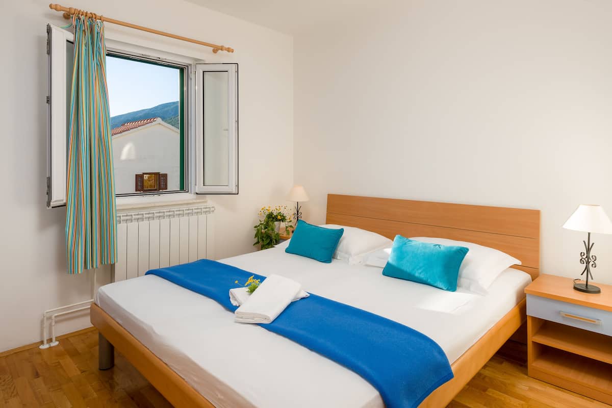 Una cama bien hecha con ropa de cama azul y blanca, un cabecero de madera y una ventana con cortinas.