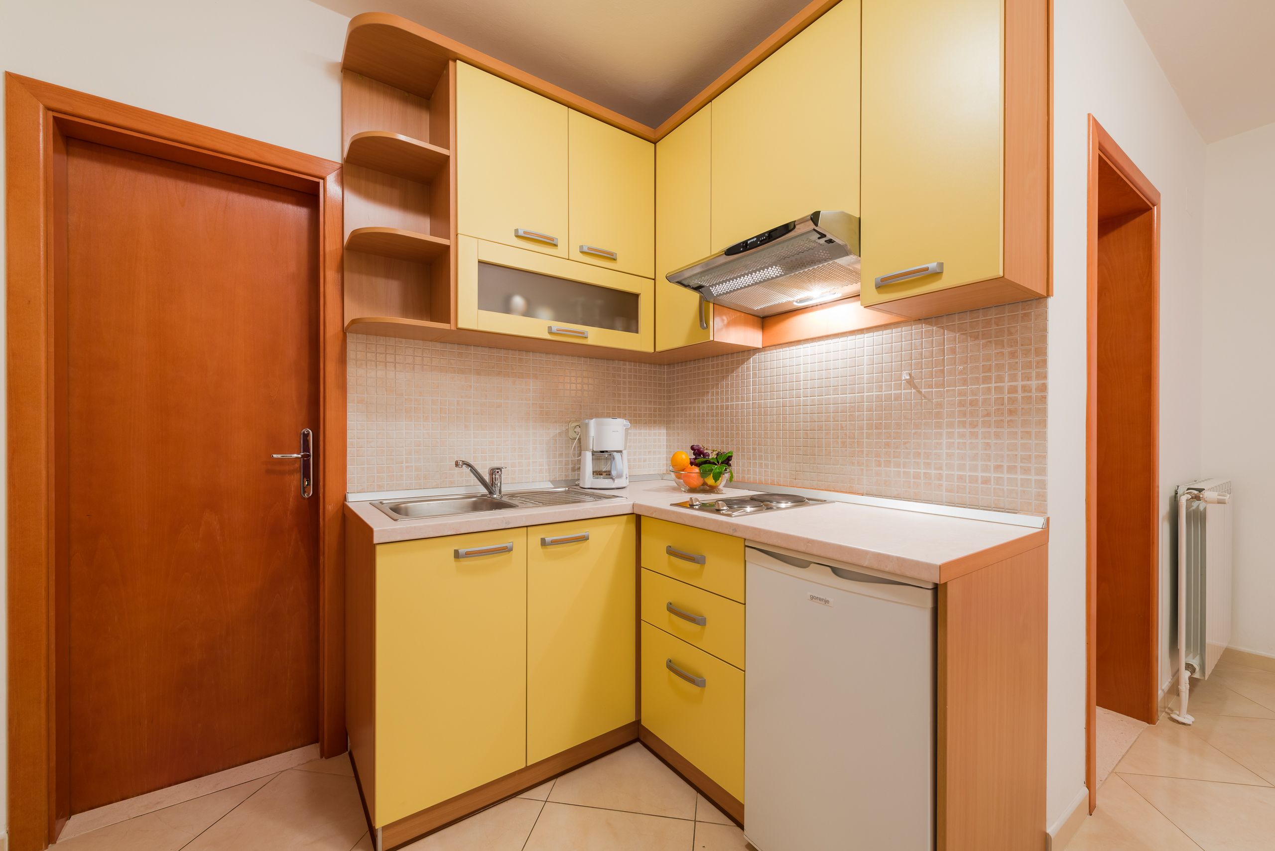 A compact kitchen with yellow cabinets, a white countertop, a built-in oven, and a dishwasher.