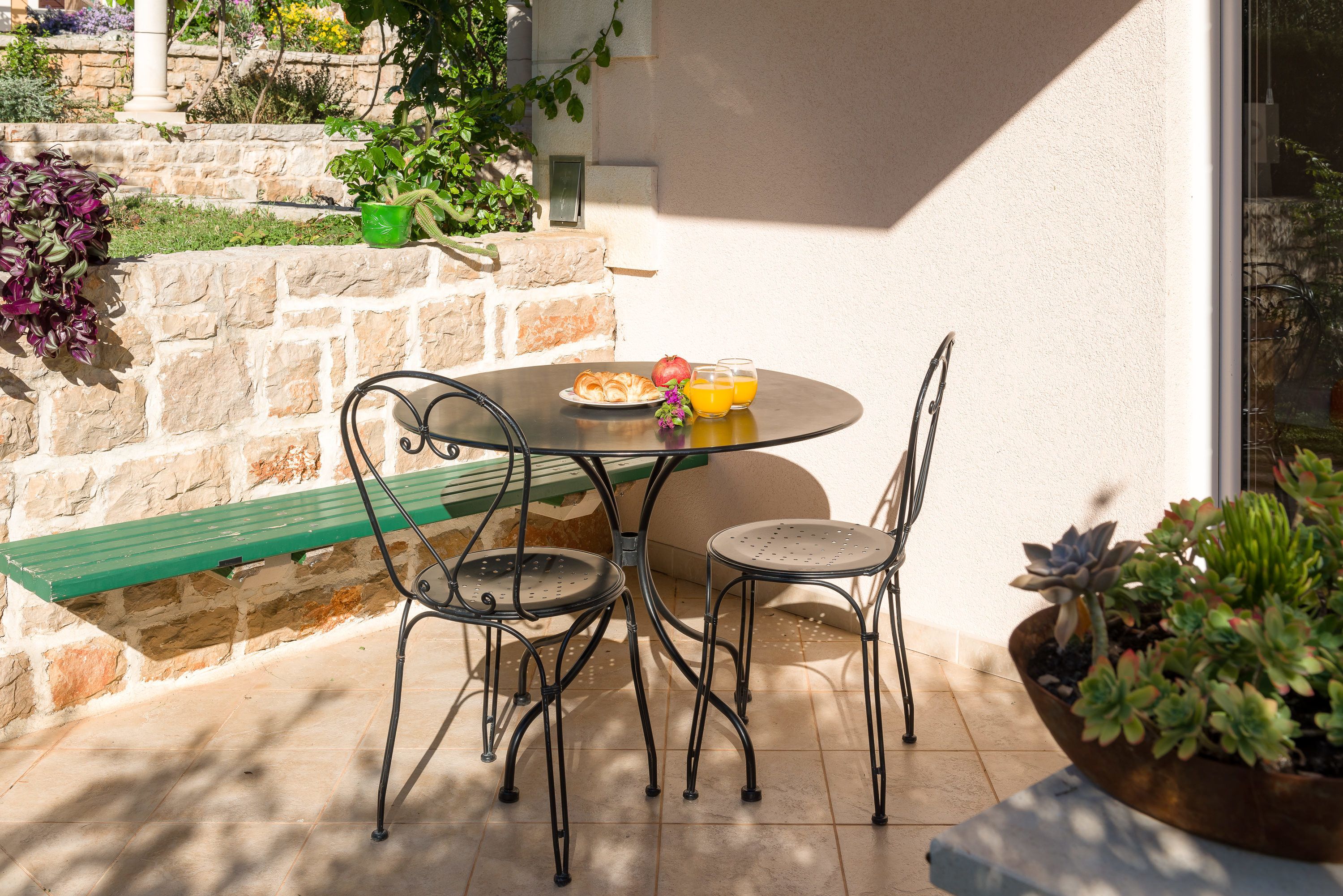 A round table with a bench, two chairs, and a plate with food and drinks.