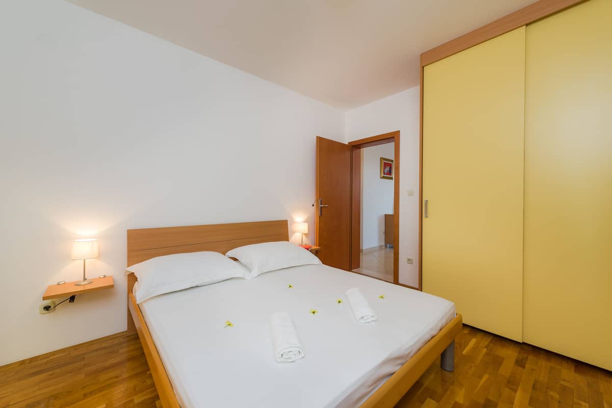 Una cama bien tendida con sábanas blancas y toallas enrolladas, una lámpara de noche y un cabecero de madera.
