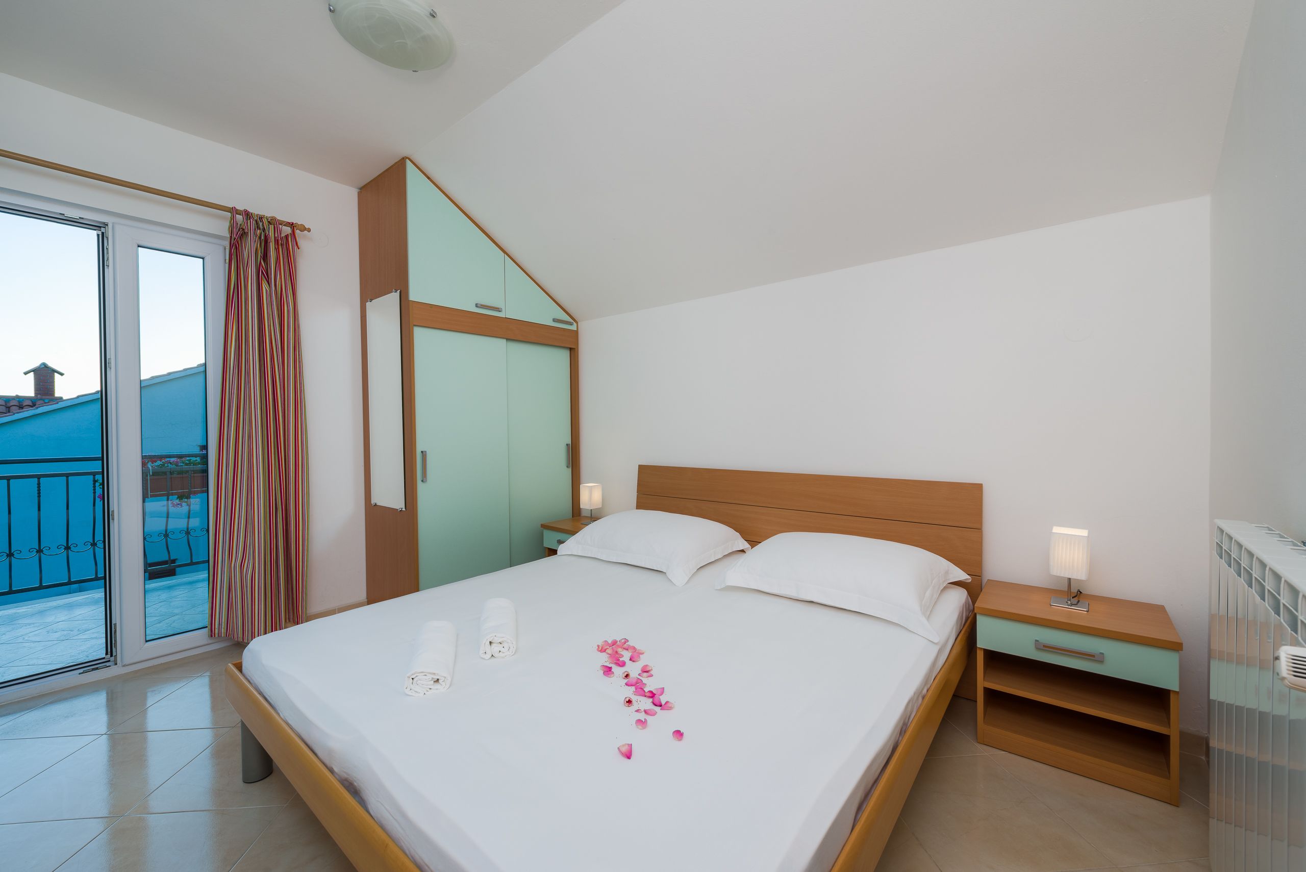 A hotel room with a bed, a nightstand, a window with curtains, and a view of the outside.