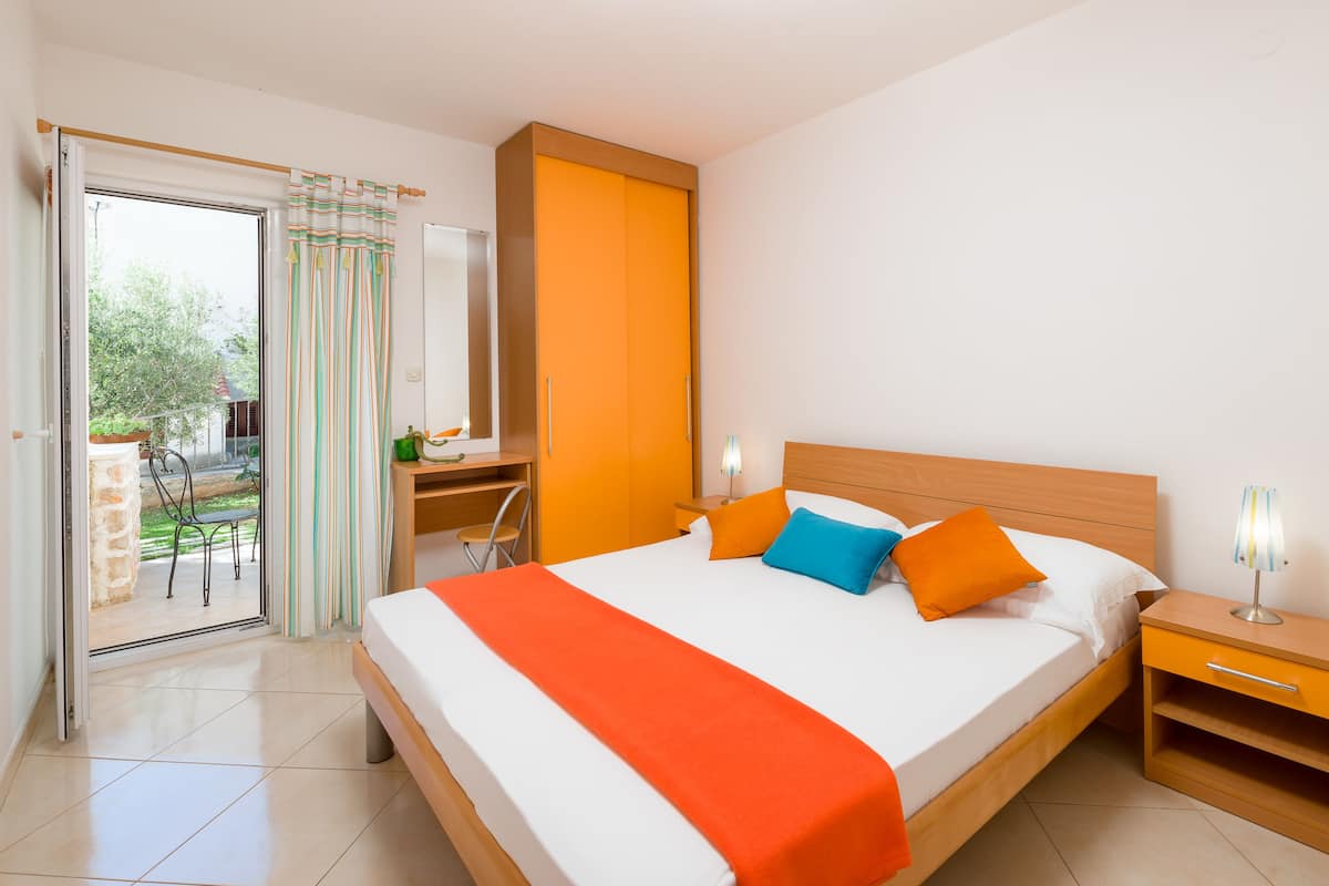 Habitación de hotel con una cama grande, una mesita de noche de madera, un escritorio con una silla y una puerta corrediza de vidrio que da a un área exterior.