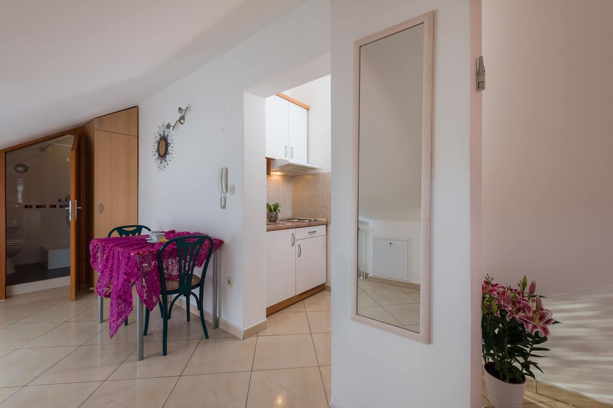 Una cocina moderna con armarios blancos, salpicadero de azulejos y un comedor con mantel rosa y sillas verdes.