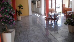 A spacious indoor area with tiled flooring, a dining table with chairs, potted plants, and a television mounted on the wall. - Pousada Porto do Sol (Cabo Frio)