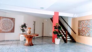 A spacious lobby with a round wooden table, a potted plant, and a staircase. - Pousada Porto do Sol (Cabo Frio)