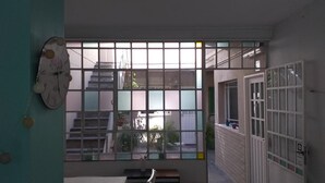 A room with a large window, a clock on the wall, and a door with a number. - Boho Rooms (Buenos Aires)