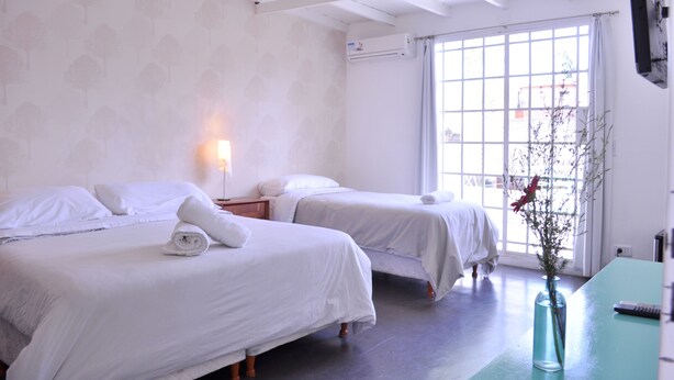 A hotel room with two beds, a nightstand, a vase with flowers, and a window with curtains. - Boho Rooms (Buenos Aires)