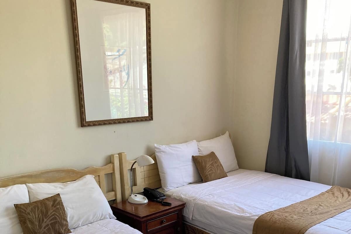 A hotel room with two beds, a bedside table with a lamp, a phone, and a mirror on the wall.