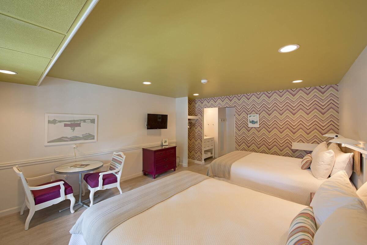 A hotel room with two beds, a desk with a chair, a television, and a bathroom visible through an open door.