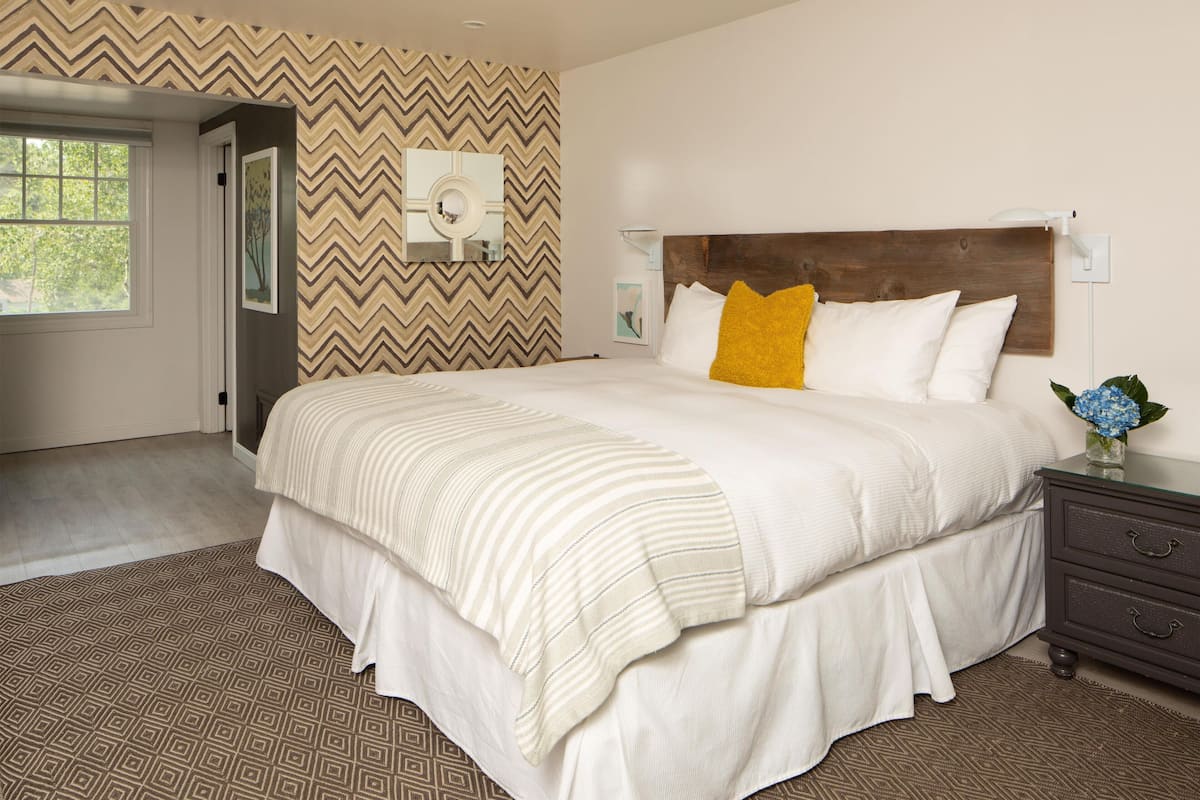 A bedroom with a large bed, a wooden headboard, a bedside table, and a patterned rug.