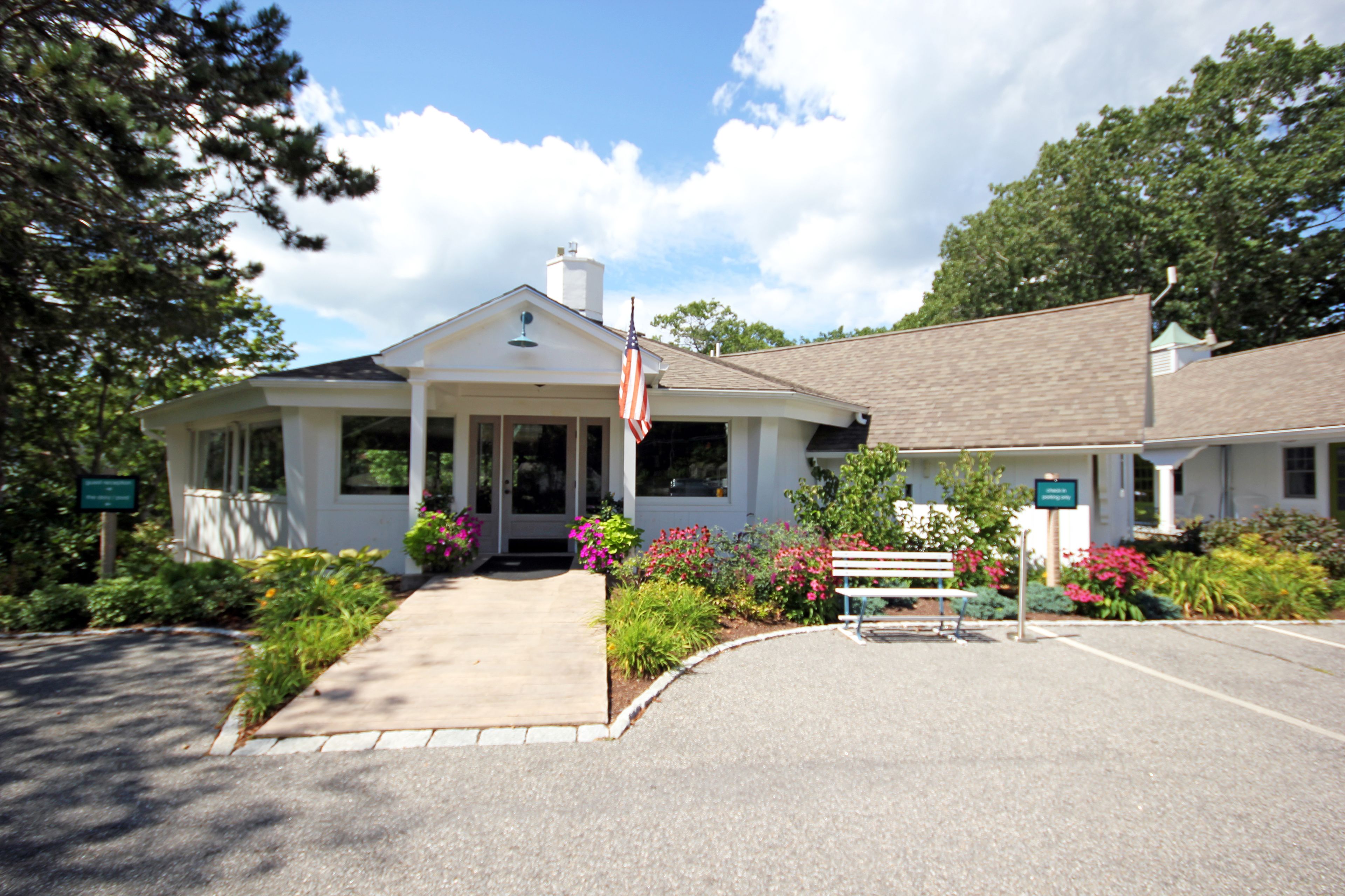 A two-story building with a white exterior, a front porch, and a flag.