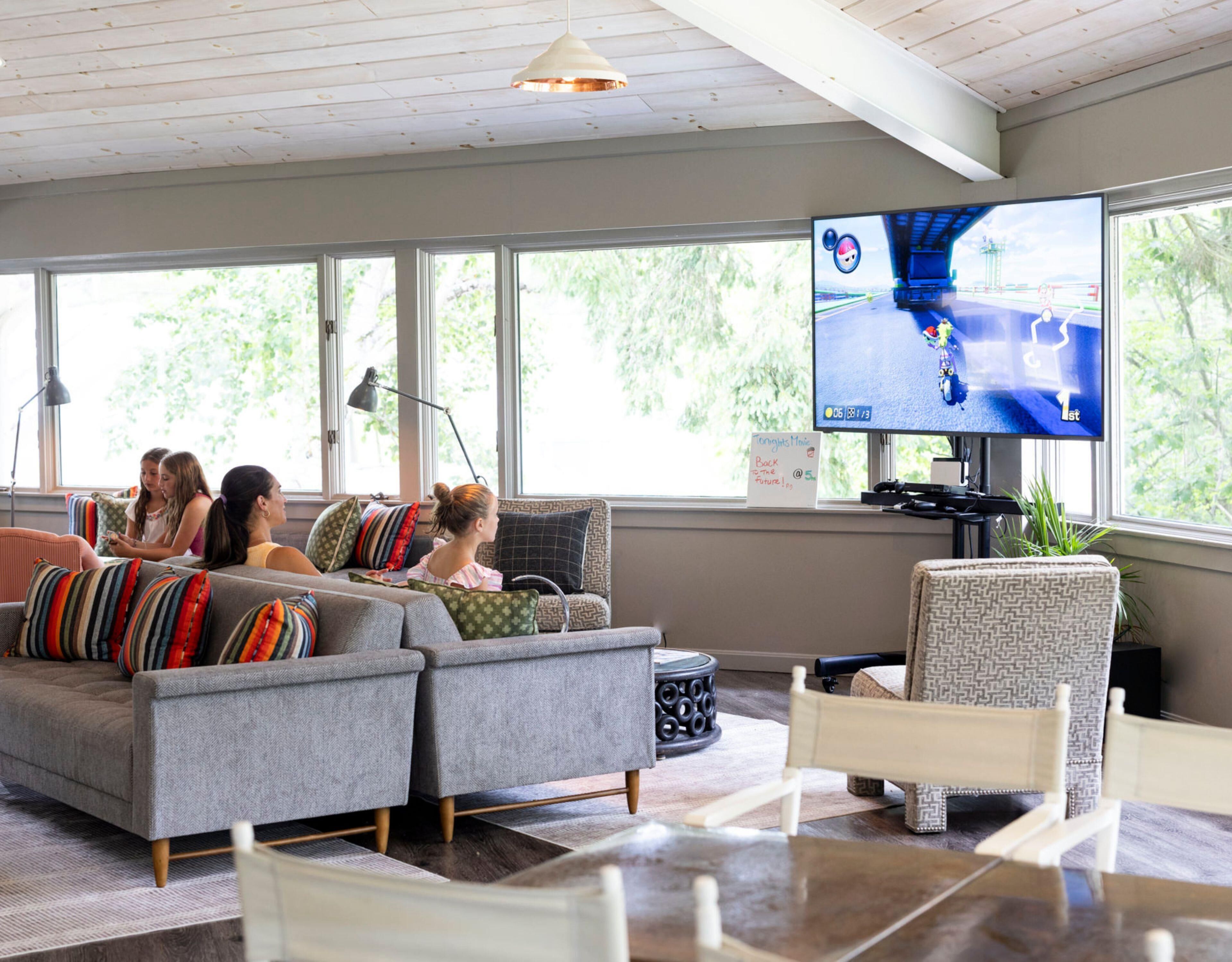 A living room with a large TV, a sofa, a chair, and a table.