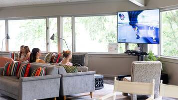 A living room with a large TV, a sofa, a chair, and a table.