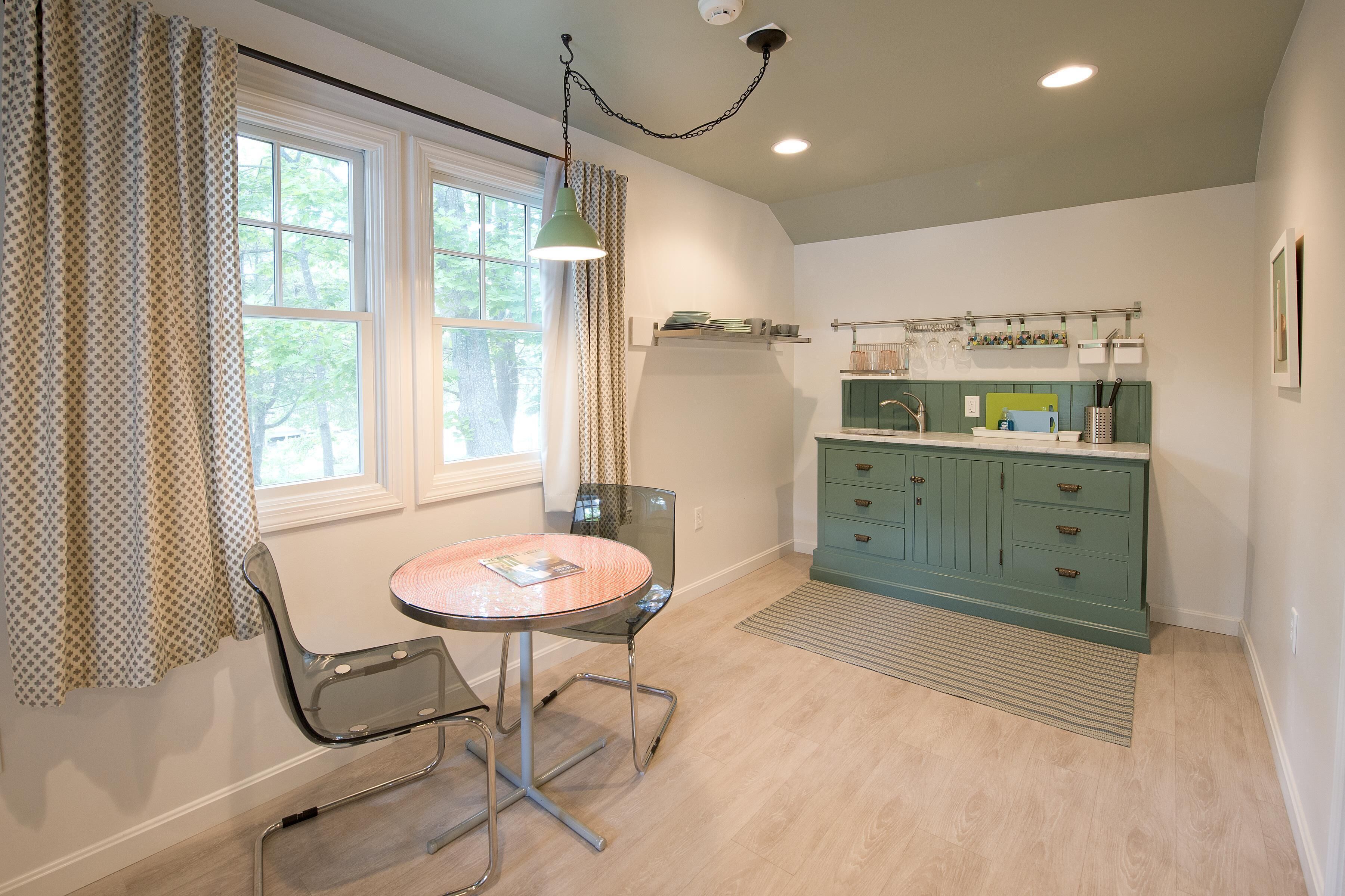 A kitchen with a dining area, featuring a table, chairs, a hanging light, and a green cabinet.