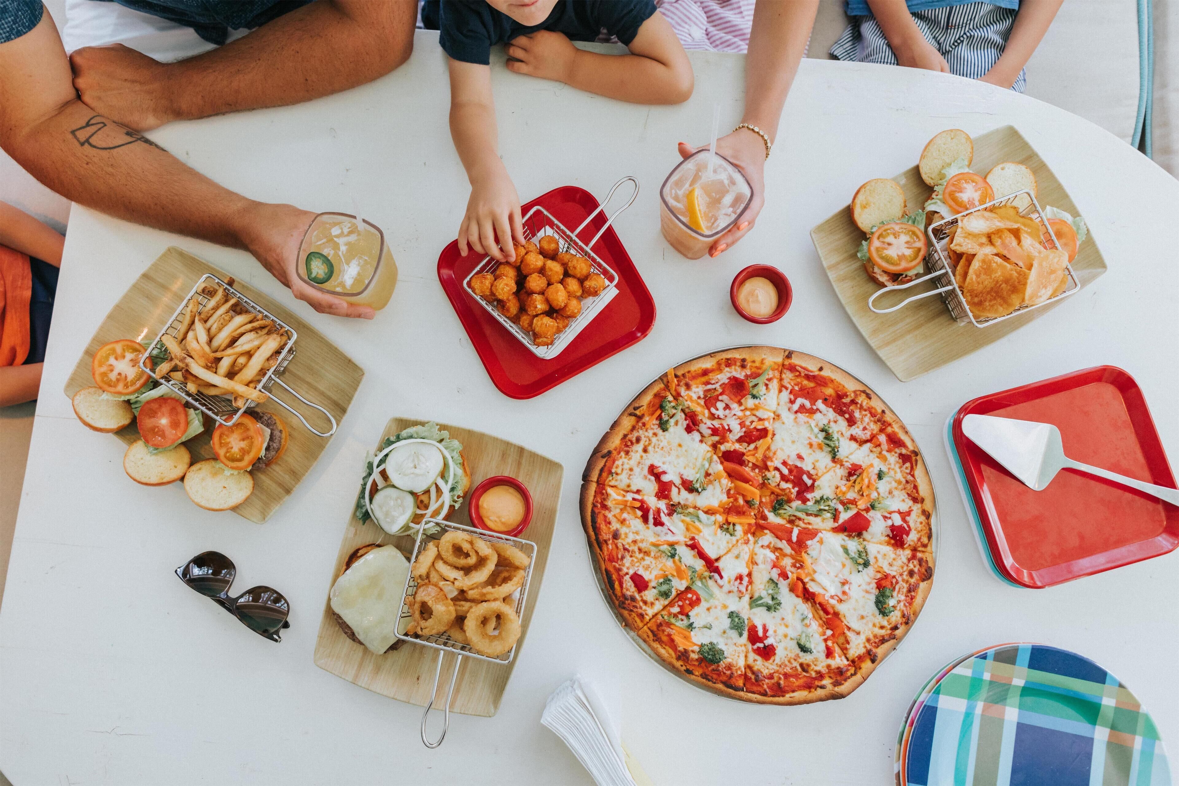 Una mesa con distintos platos, como pizza, papas fritas, aros de cebolla y pan.