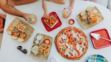 Una mesa con distintos platos, como pizza, papas fritas, aros de cebolla y pan.