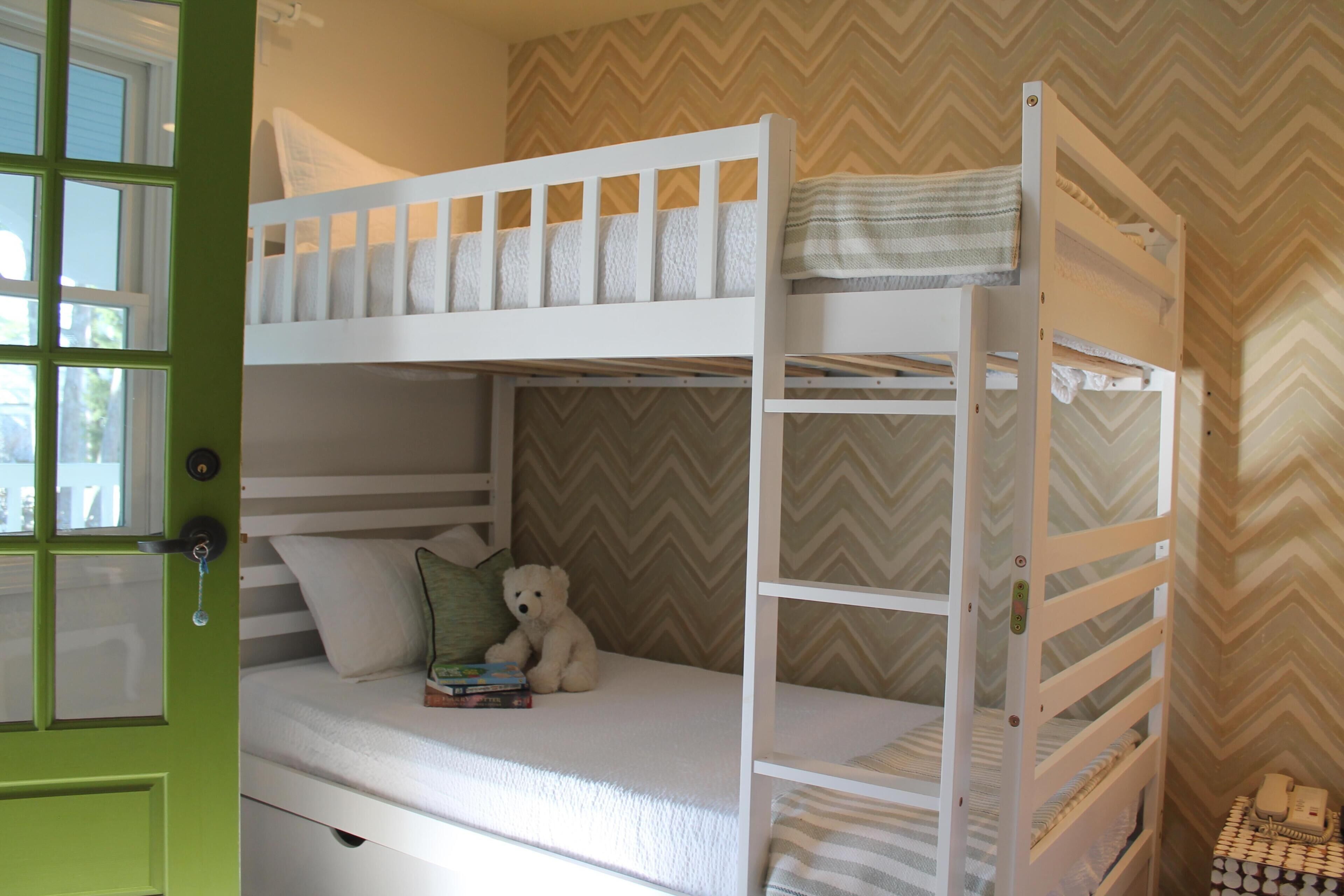 Habitación con literas, una puerta verde, un osito de peluche y una pequeña mesa con un teléfono.