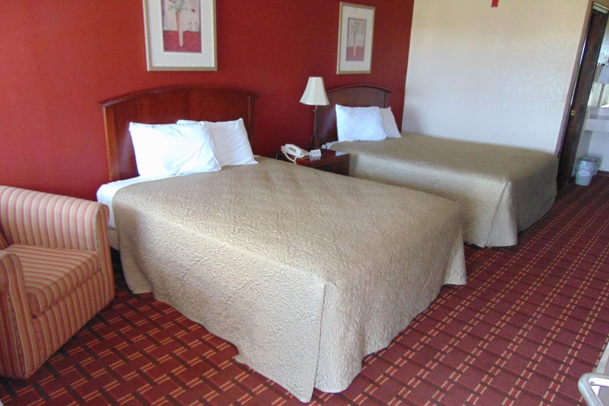Habitación de hotel con dos camas, una silla y piso cubierto con alfombra roja.