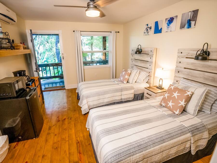 A bedroom with two beds, a refrigerator, a microwave, and a ceiling fan.