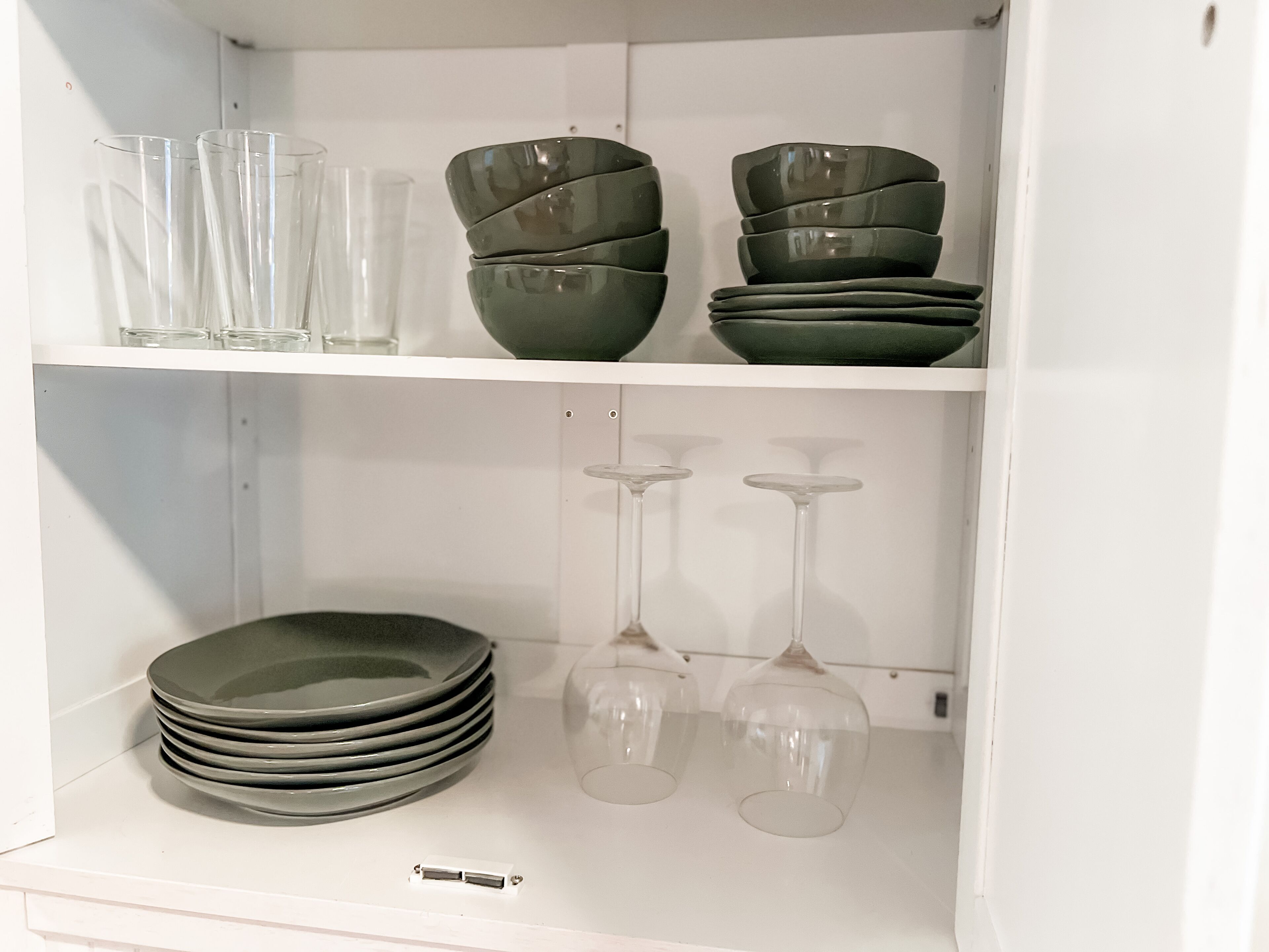 A white shelf with clear glasses, stacked bowls, and wine glasses.