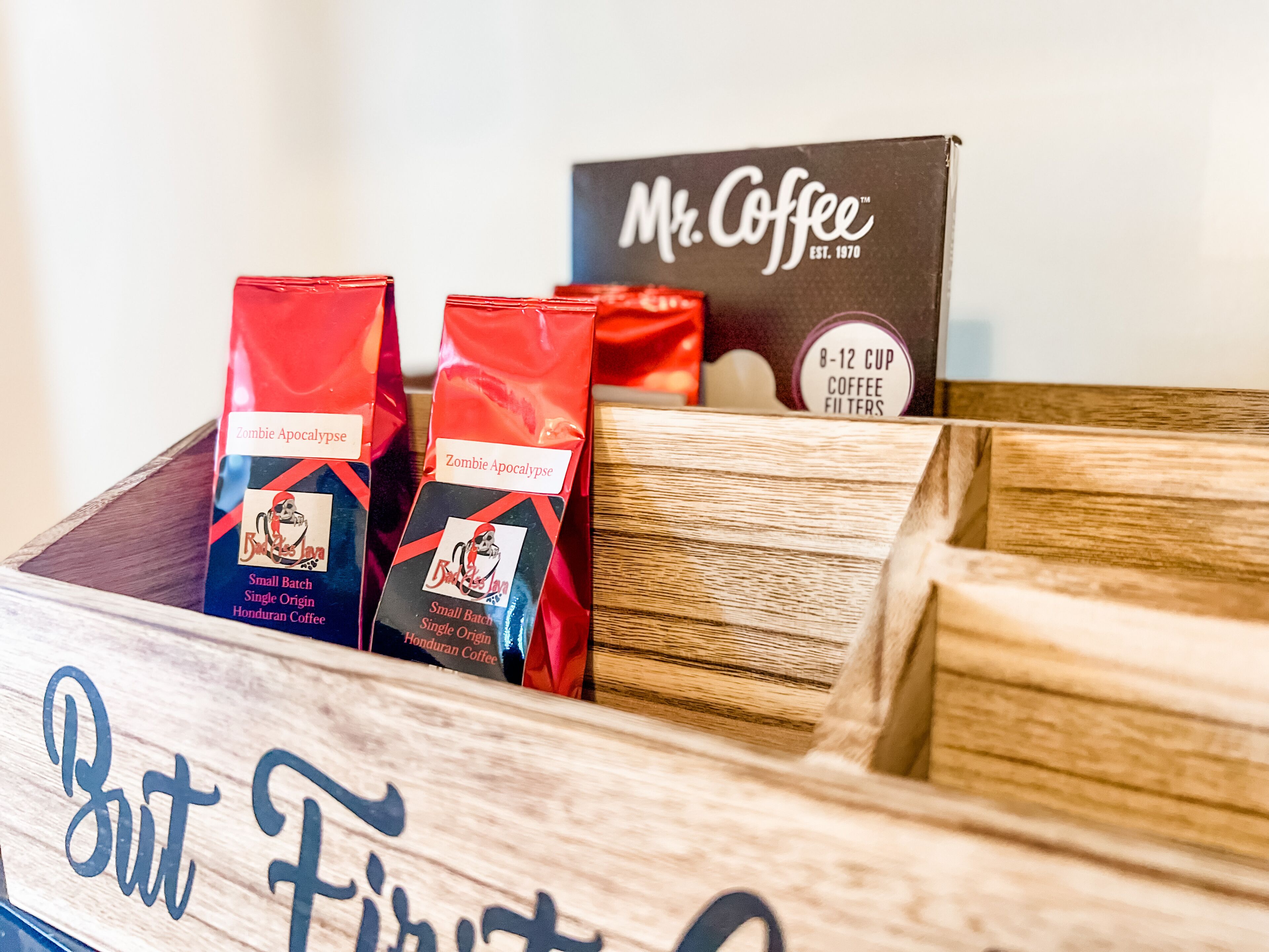 Uma caixa de madeira com sacos de café rotulados 'Zombie Apocalypse' e uma caixa de 'Mr. Coffee'.