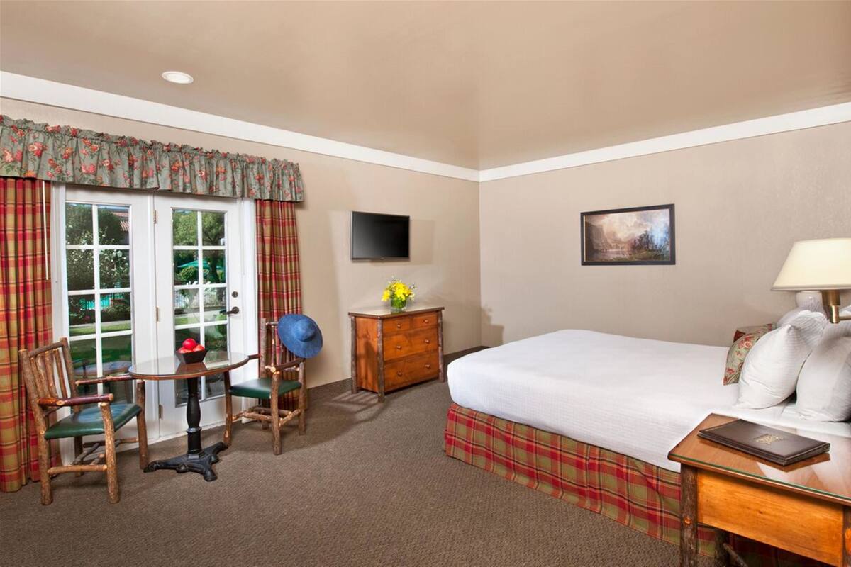 A hotel room with a bed, a desk with a chair, a dresser, a television, and a window with curtains.