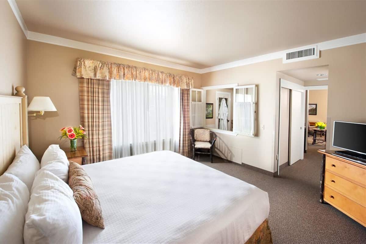 A hotel room with a large bed, a chair, a desk with a TV, and a bathroom visible through an open door.