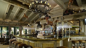 Una zona de bar con mostrador de madera, taburetes y una lámpara de araña.