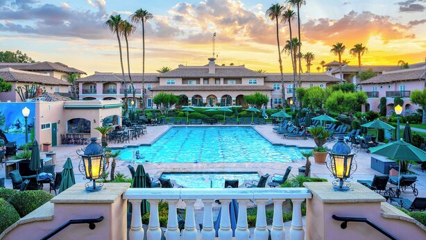 A resort with a swimming pool, lounge chairs, and a building with a tiled roof.