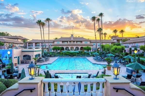 A resort with a swimming pool, lounge chairs, and a building with a tiled roof.
