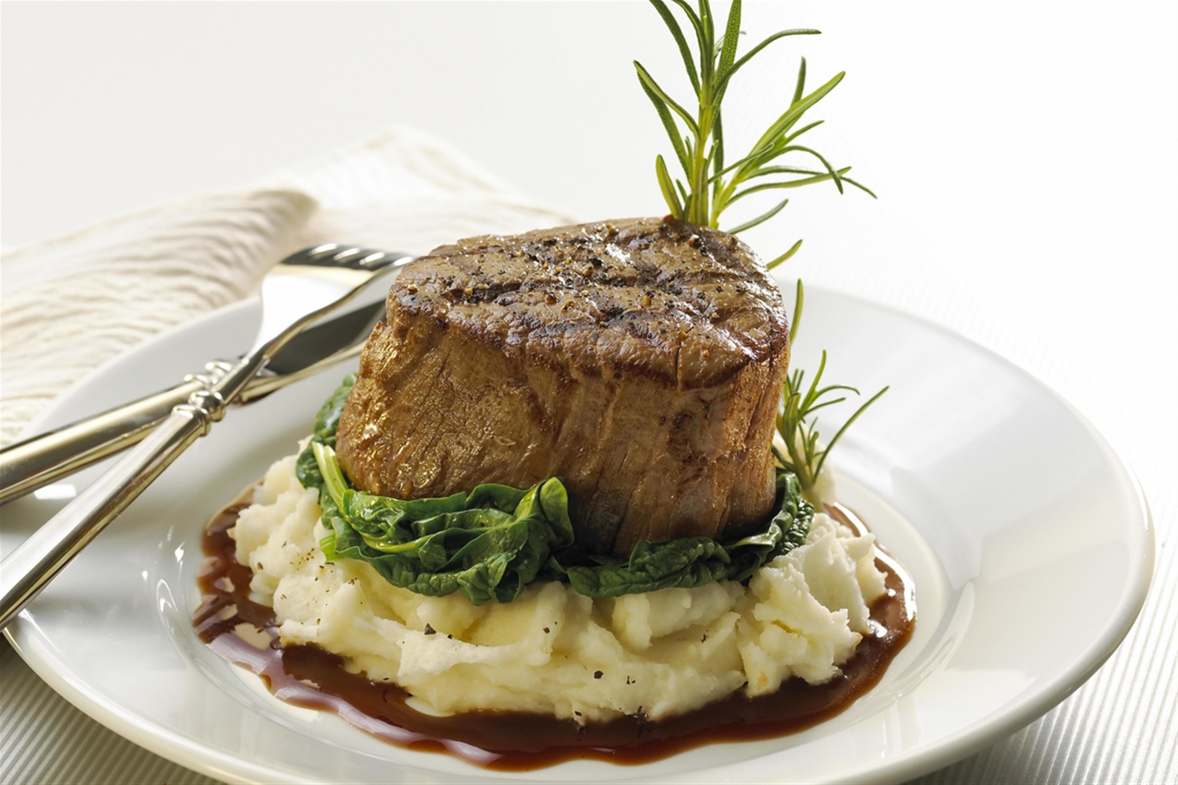 A plate with a steak, mashed potatoes, and a sprig of rosemary.