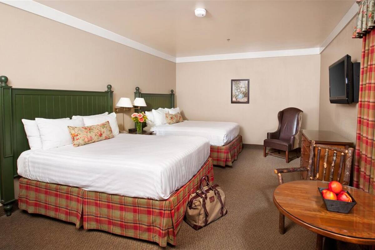 A hotel room with two beds, a chair, a table with fruit, and a TV on the wall.