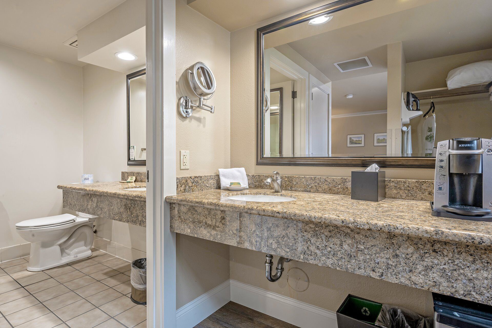 A bathroom with a toilet, sink, mirror, and coffee maker.