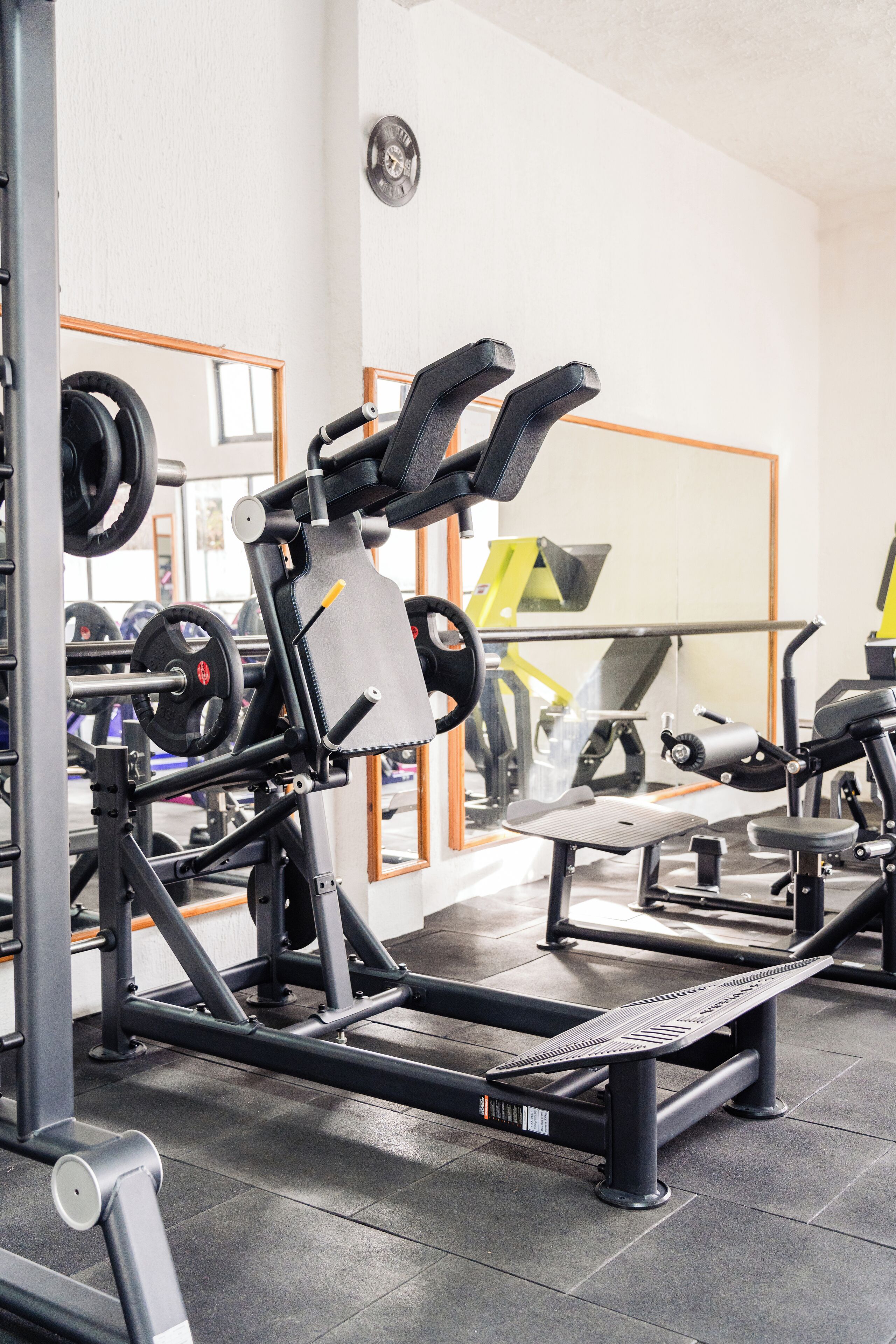 A gym with weightlifting equipment, a bench press, and a mirrored wall.