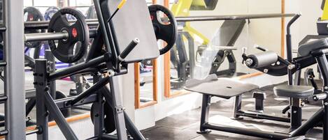A gym with weightlifting equipment, a bench press, and a mirrored wall.