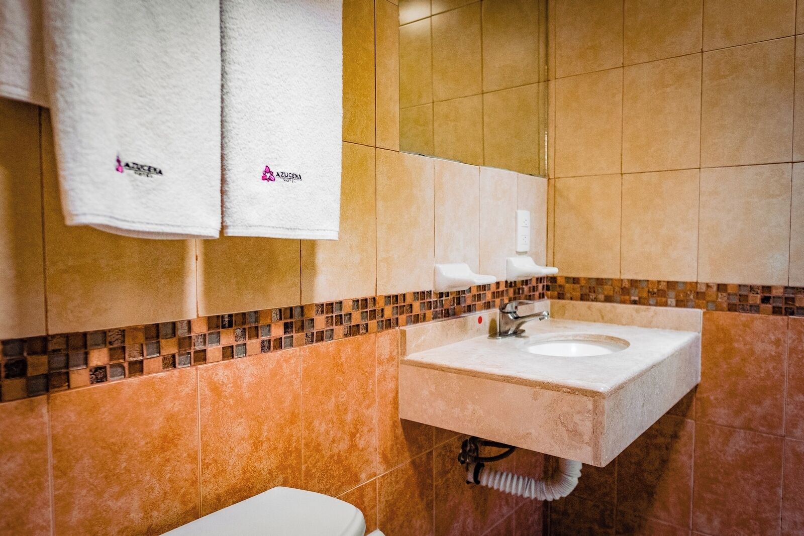 Un baño con lavamanos, dos toallas blancas colgadas en un perchero y un salpicadero de azulejos.