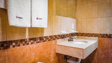 Un baño con lavamanos, dos toallas blancas colgadas en un perchero y un salpicadero de azulejos.