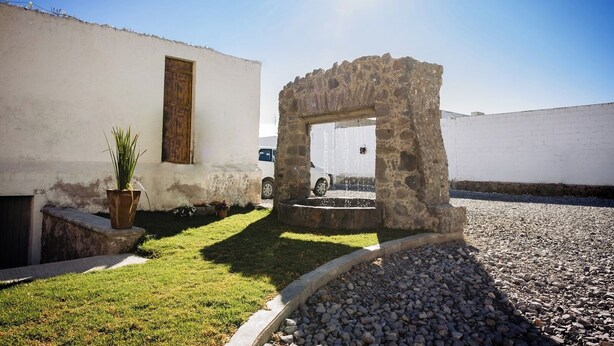 A stone archway leading to a white building with a wooden door, surrounded by a gravel path and a small grassy area. - Hotel Azucena (Huamantla)